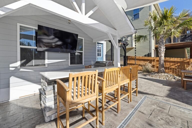 Outdoor Patio Furniture, Covered outdoor bar area with wooden bar stools, a mounted TV, stone counter