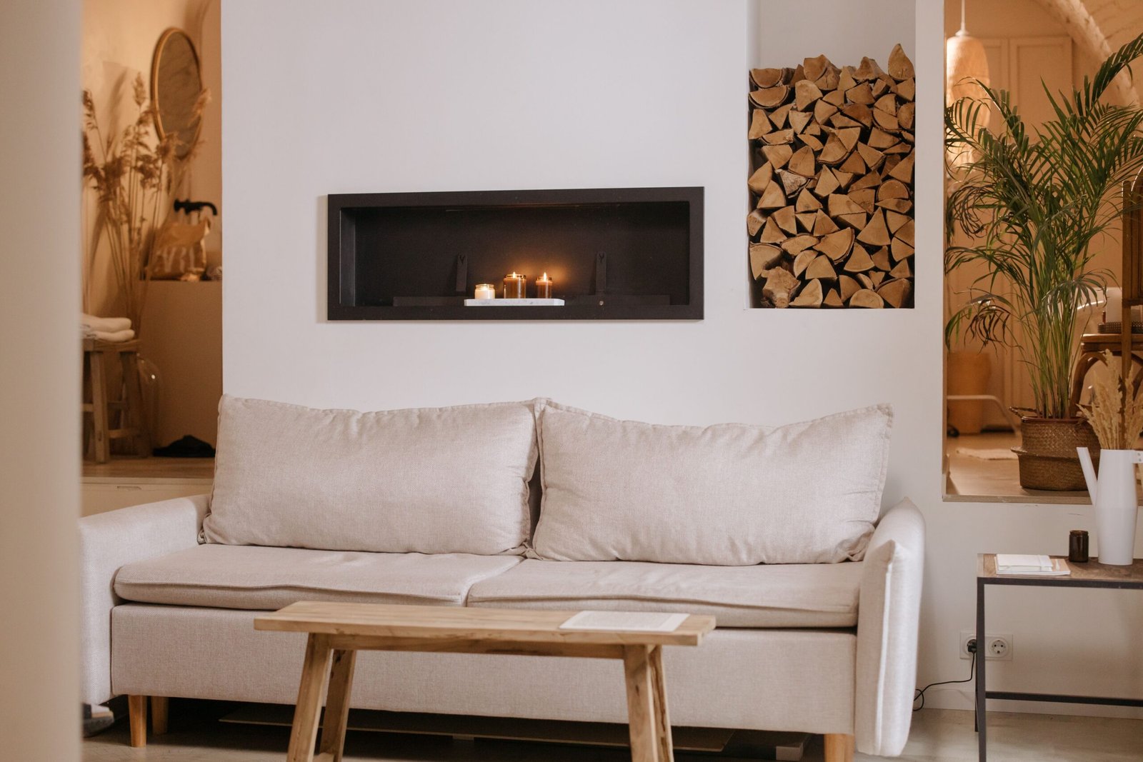 A cozy living room showcasing simple home decor ideas with a soft beige sofa, warm candle lighting, natural wood accents, and plants that create a calm and inviting atmosphere.