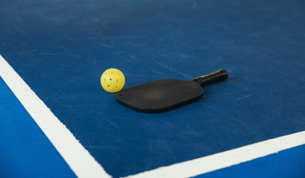 A pickleball paddle and ball on a blue court, highlighting pickleball benefits such as improved agility, coordination, and overall fitness.