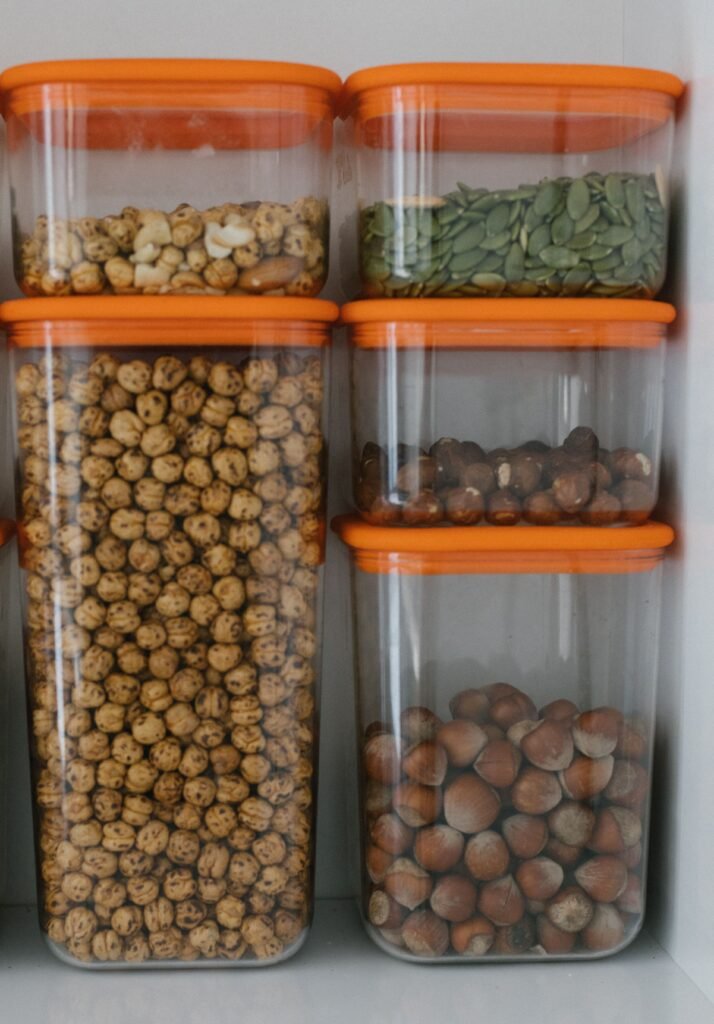   
Kitchen Storage and Organisation containers neatly arranged on a shelf, showing labeled transparent bins with dry foods like nuts and seeds for a tidy, efficient pantry.