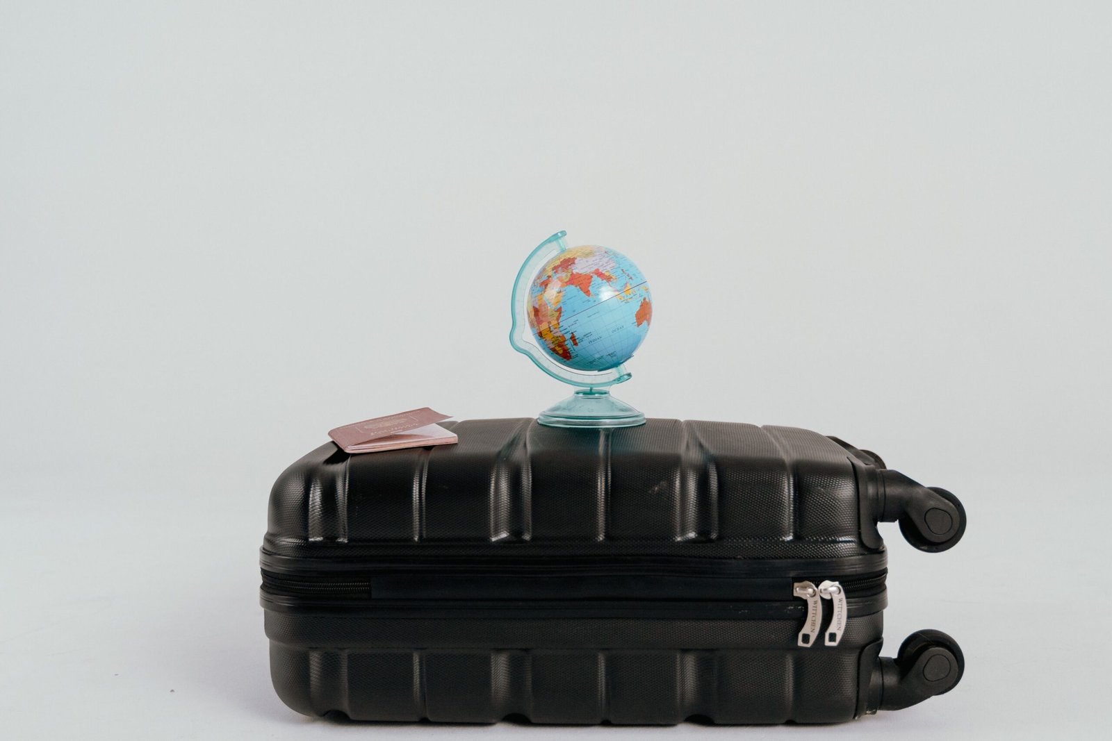 A small globe and two passports placed on a closed suitcase, symbolizing how traveling helps you heal mentally after years of working from home.