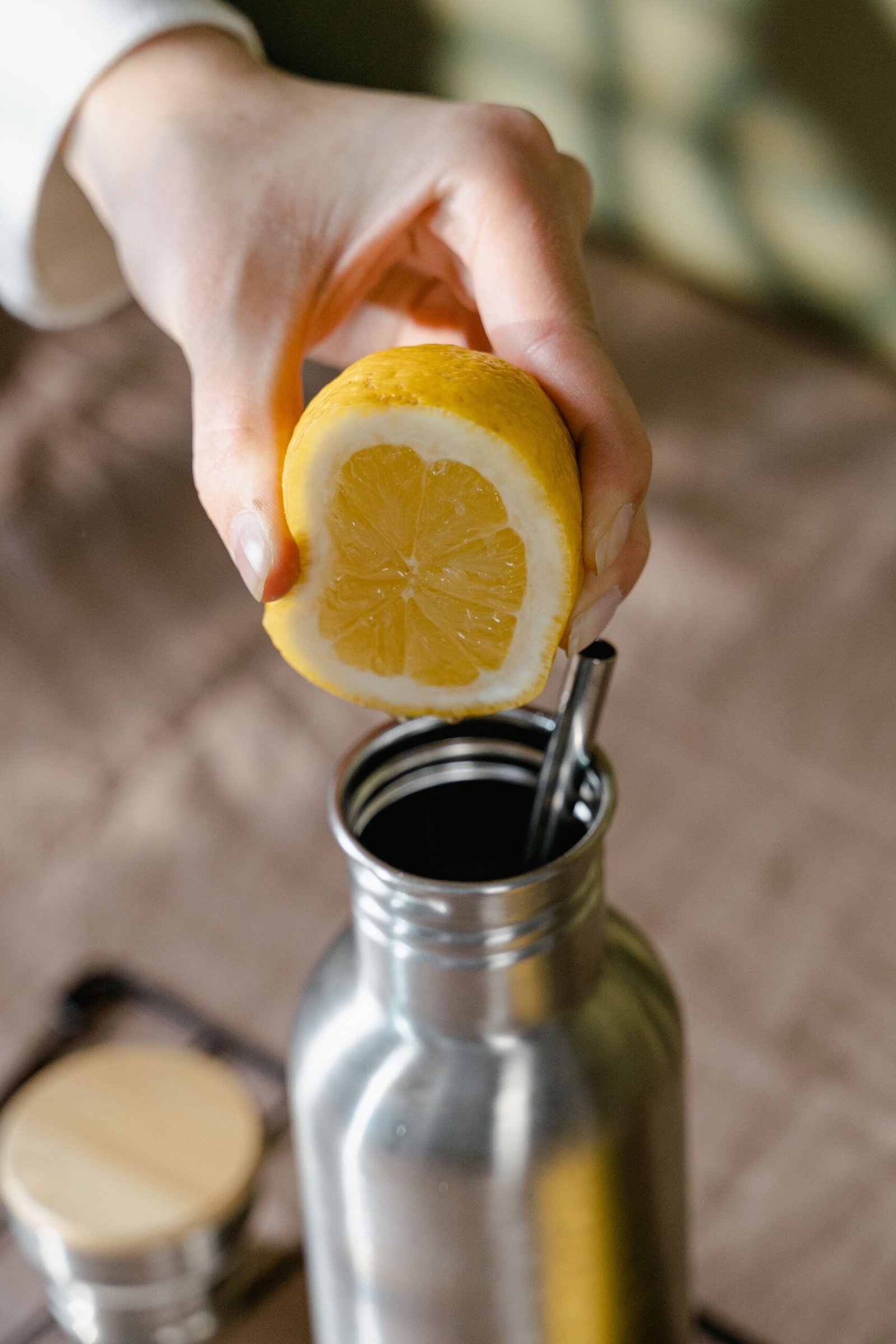 Hand squeezing fresh lemon into a stainless steel water bottle as part of Daily Wellness Routines for Organic Living.