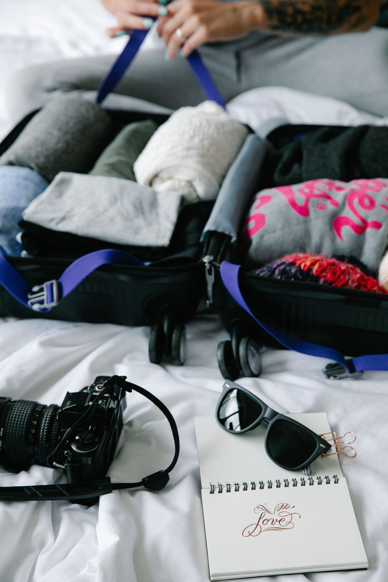 Open suitcase with neatly rolled clothes, camera, sunglasses and notebook as part of Travel Essentials You Actually Need.