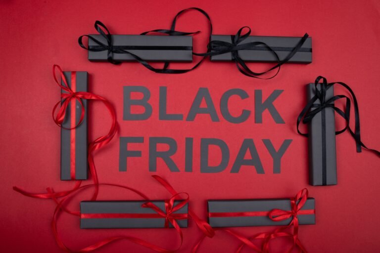 The words Black Friday in black letters on a red background, framed by slim black gift boxes tied with black and red ribbons