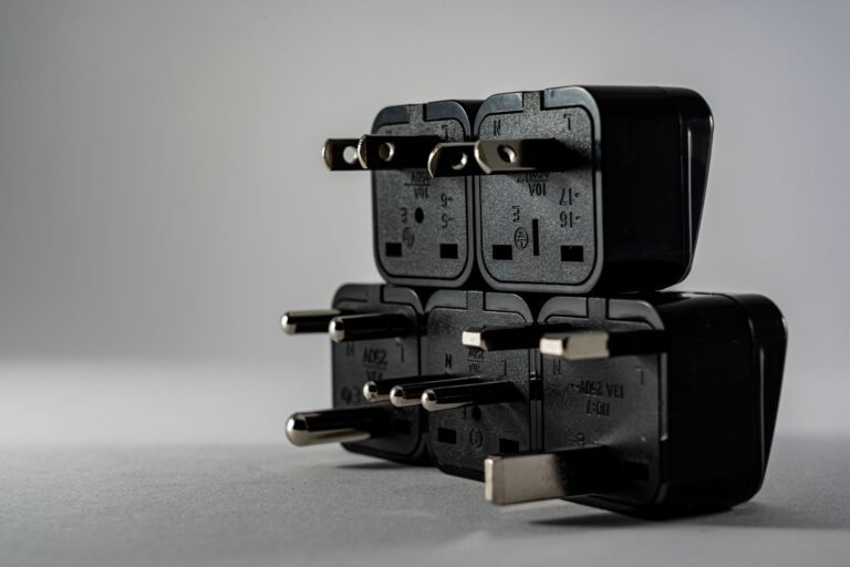 Stack of black travel plug adapters with different prong styles, including flat, round and rectangular pins, on a grey surface
