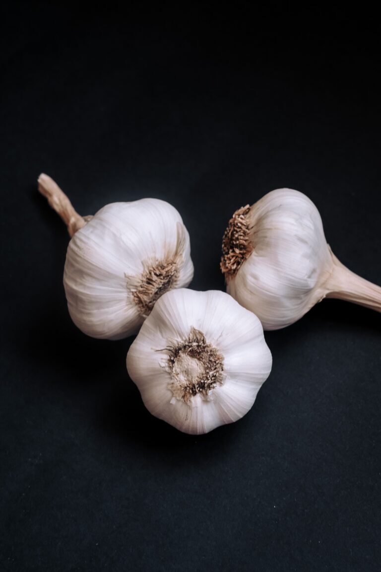 Three whole garlic bulbs with papery white skins and dry root ends on a dark background